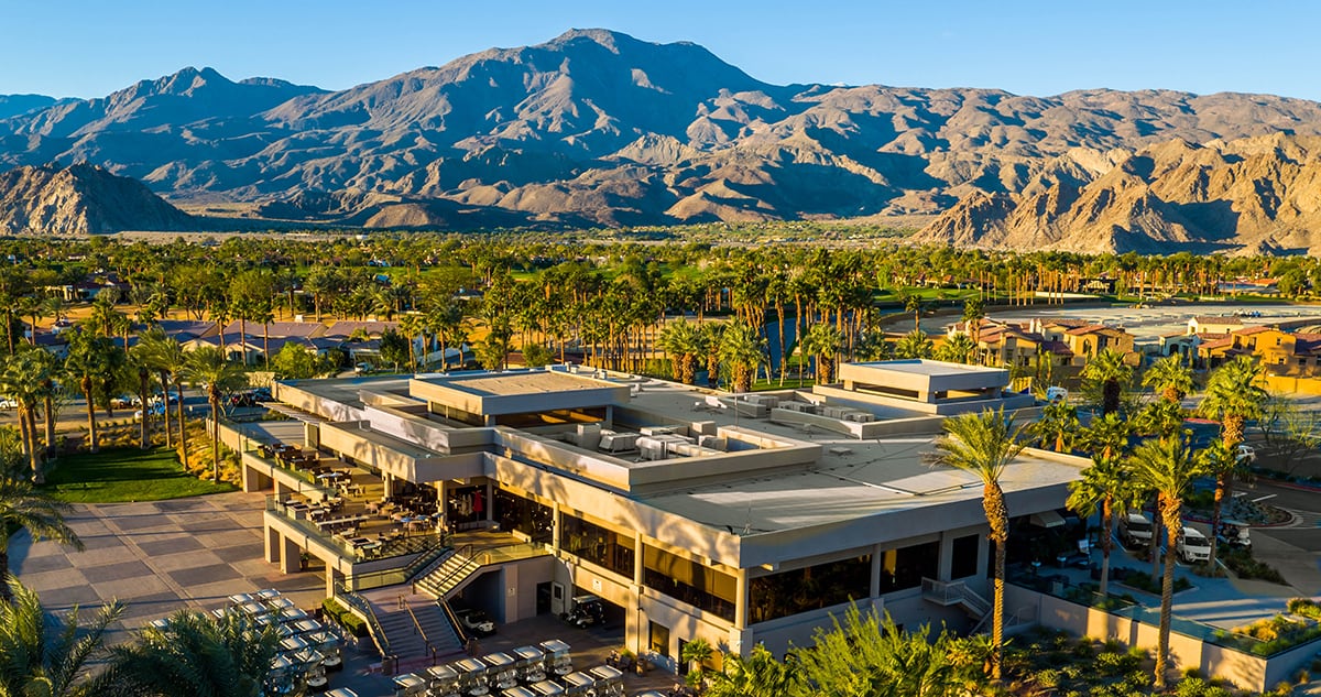 A modern resort with a pool, surrounded by palm trees, with mountains in the background under a clear sky.