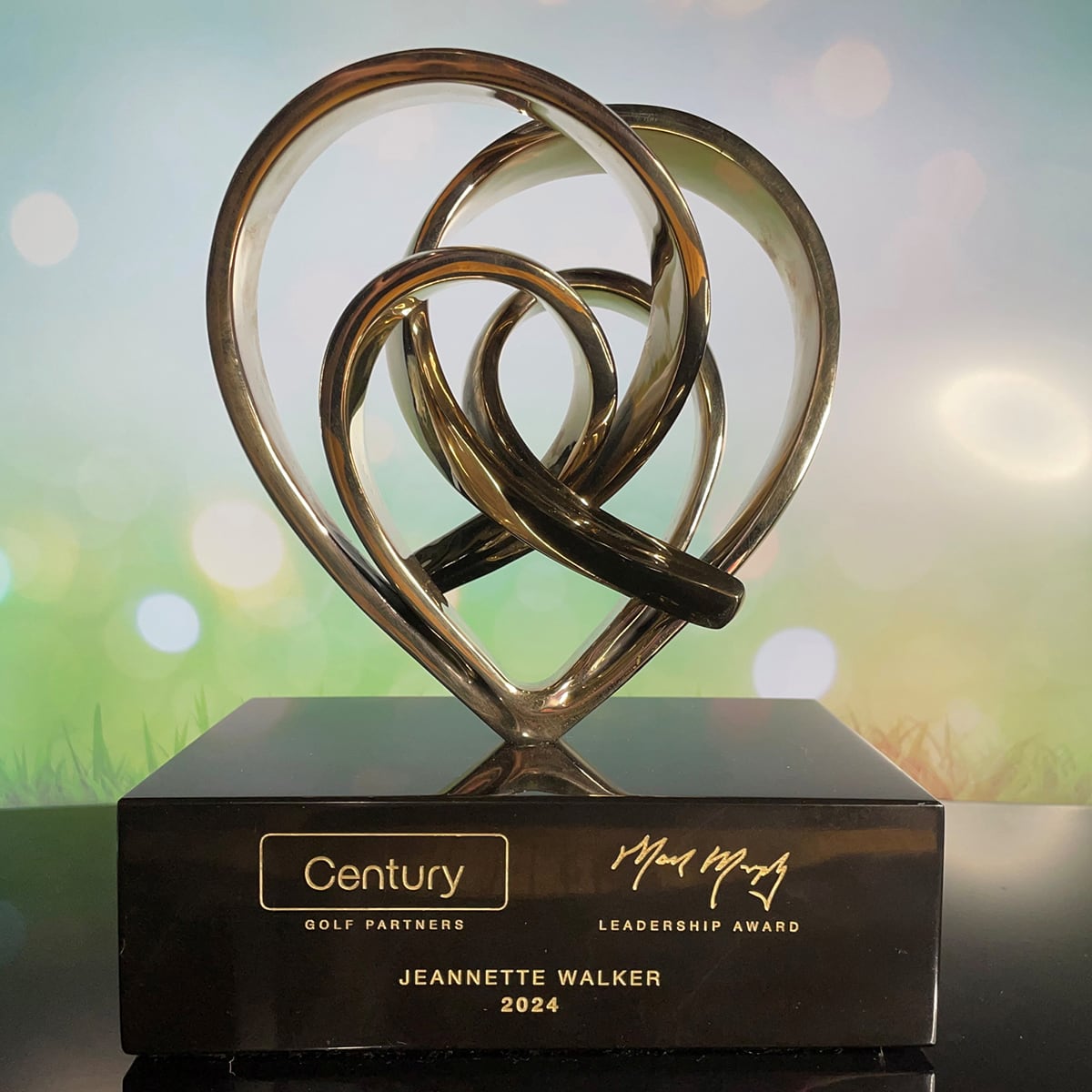 A metallic heart-shaped sculpture award sits on a black base engraved with Jeannette Walker 2024.
