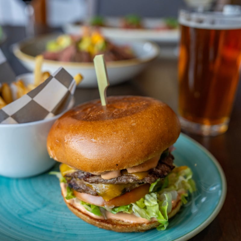 Burger with lettuce, tomato, cheese, and sauce on a bun, served with fries and a glass of beer.