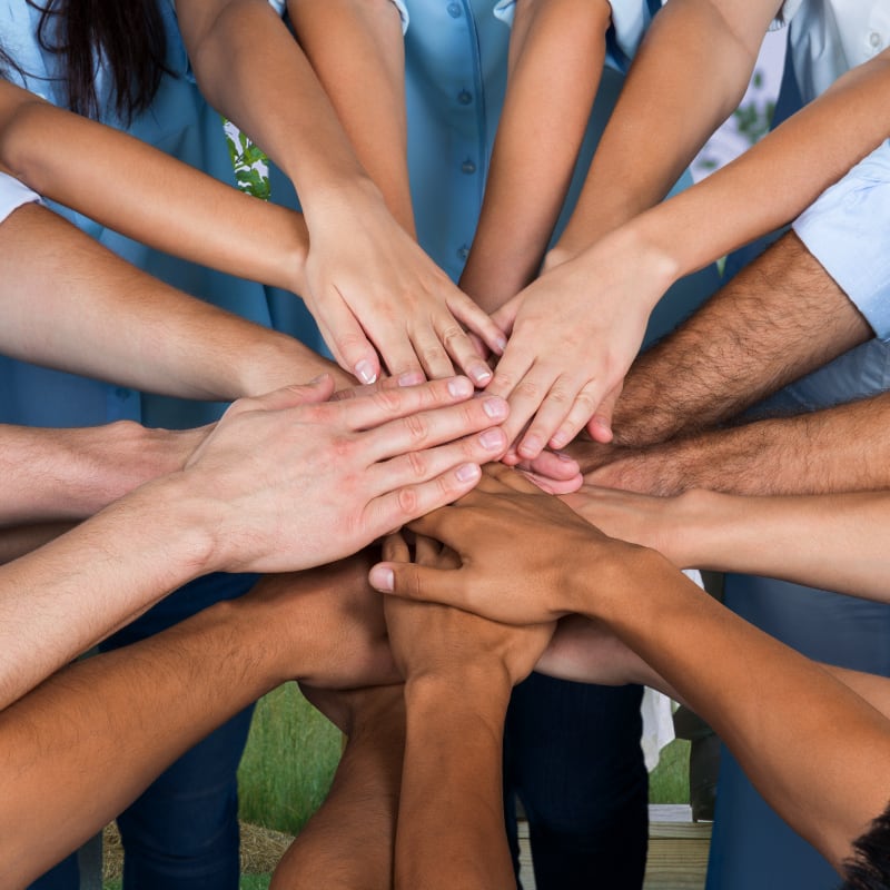 Several people stacking their hands together in the center, symbolizing teamwork and unity.