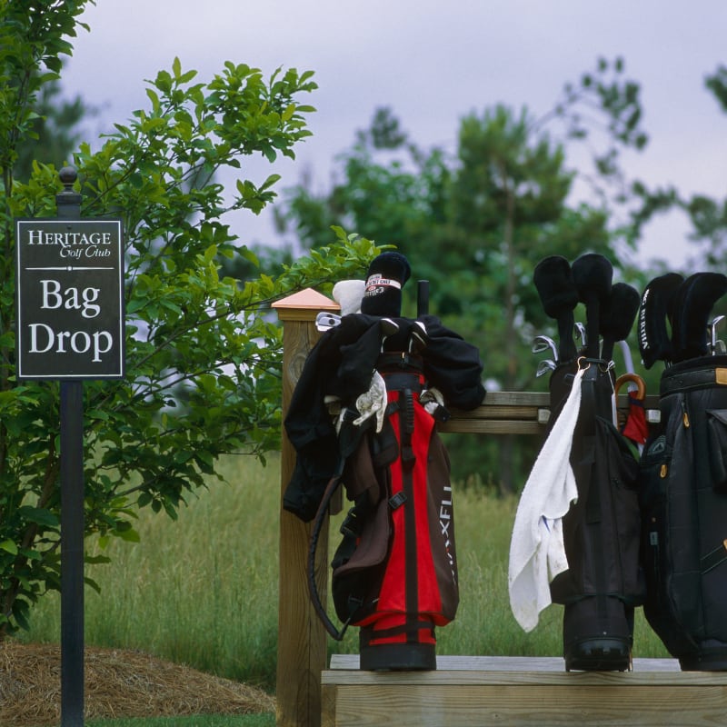 Several golf bags hang on a wooden rack near a Bag Drop sign at a golf course.