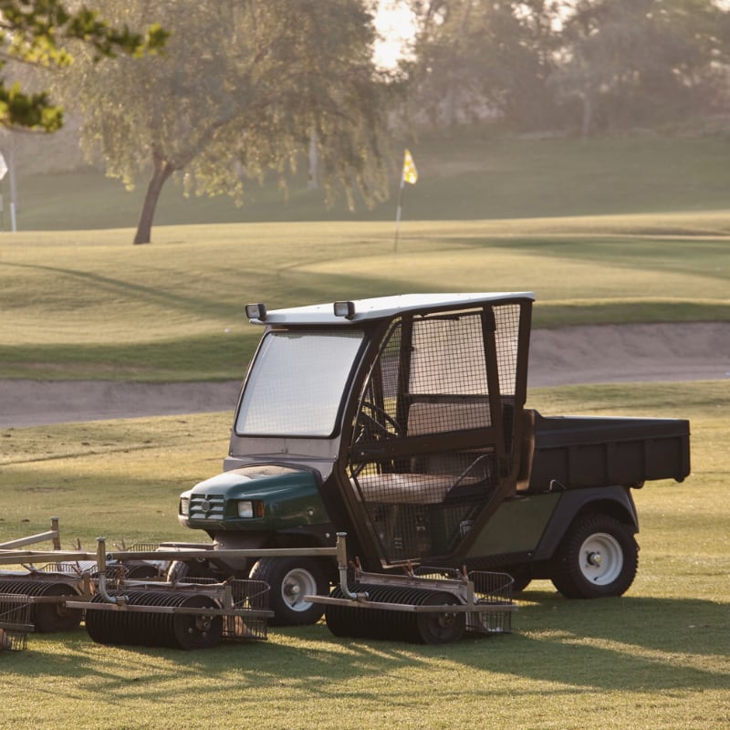 A green utility cart and turf maintenance equipment on a golf course in the early morning light.