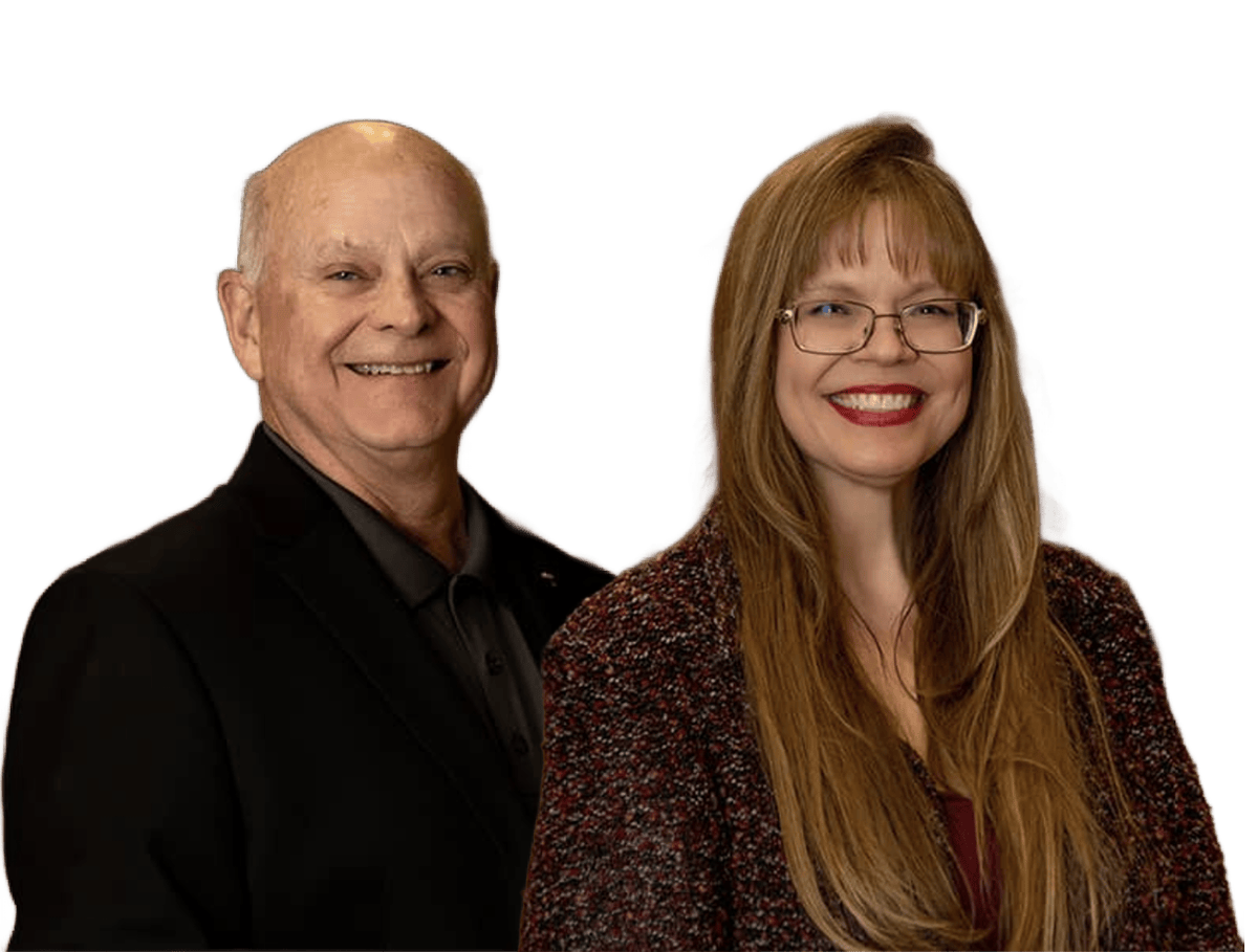 Two people standing and smiling, one older man in a suit and one woman with long hair and glasses.