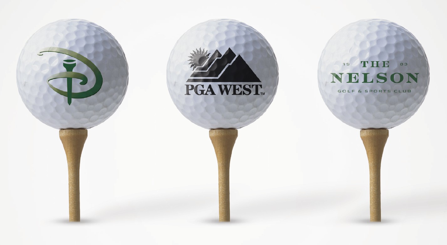 Three golf balls on tees, each with a different golf club logo printed on the front.