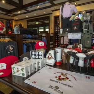 Golf shop display with hats, shirts, golf balls, headcovers, and a towel reading Grumpys Gauntlet.