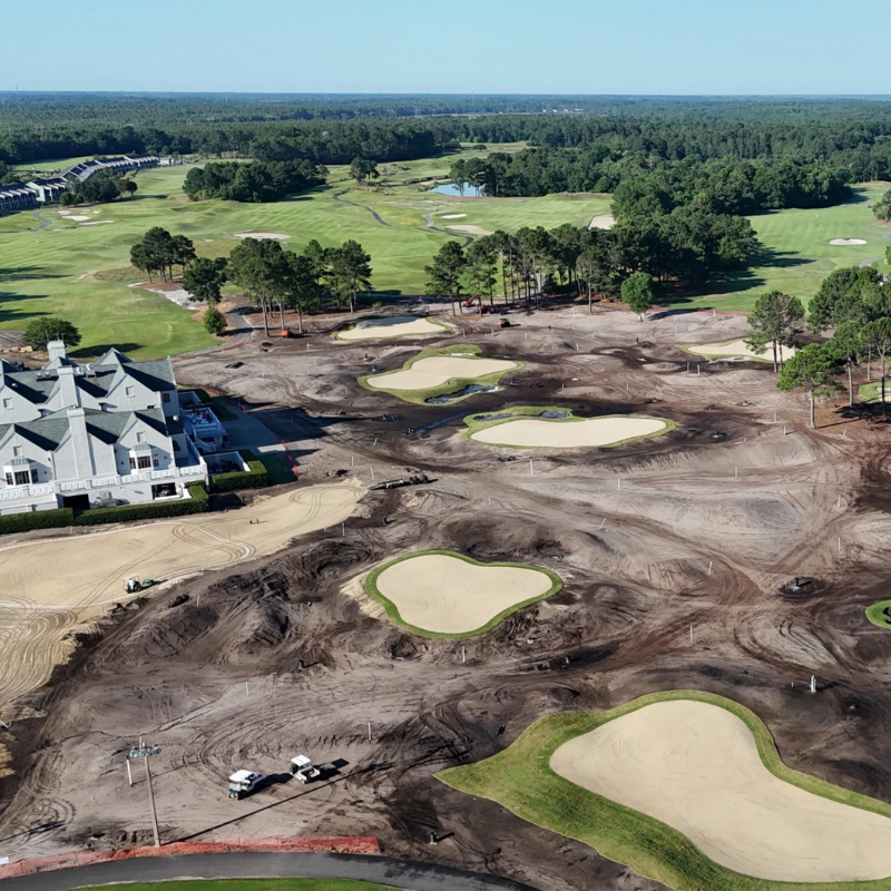 Aerial view of a golf course under renovation with exposed dirt, sand traps, and some green grass.