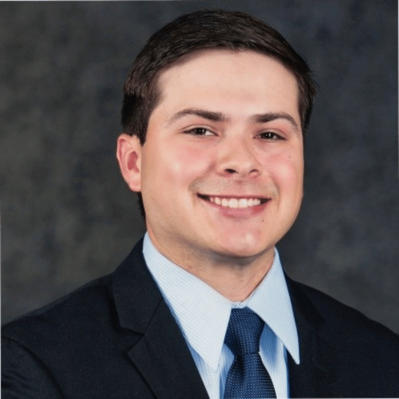 Smiling man in a suit and tie poses against a dark, textured background.