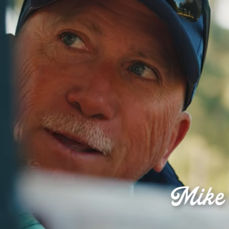A man in a blue cap looking to the side, with Mike written in white cursive text at the bottom right.